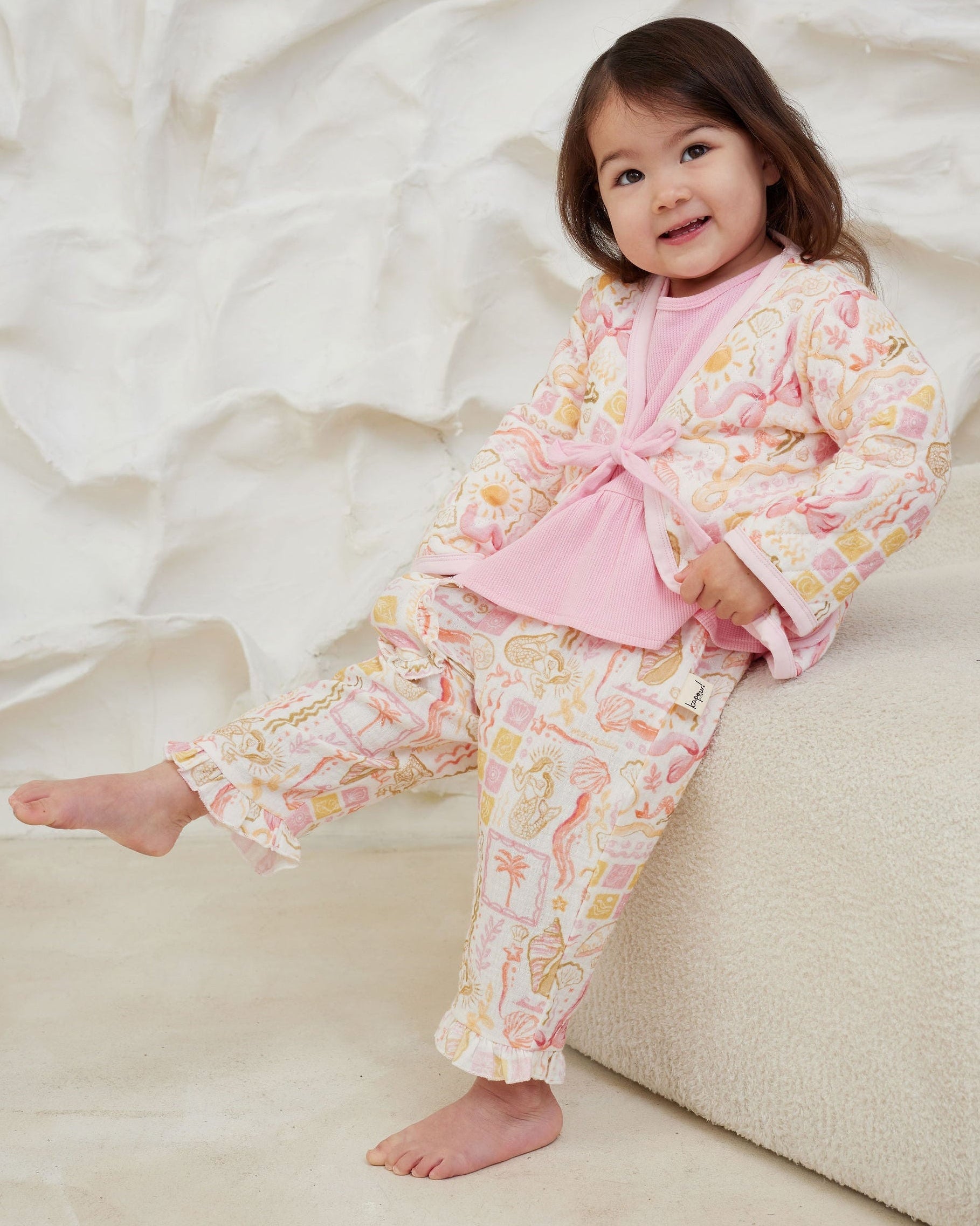 Child wearing a pink and floral outfit sitting on a white surface